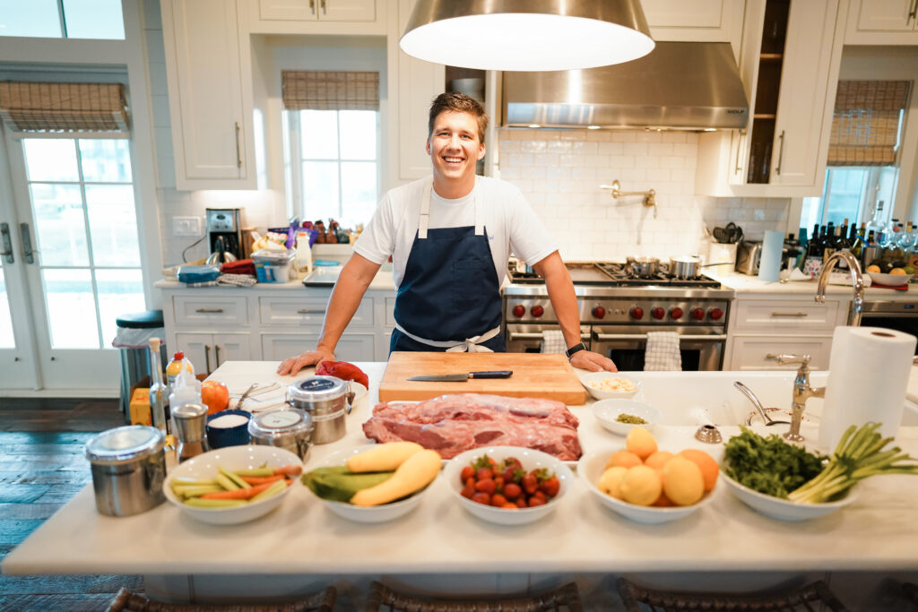 Chef Nathan Davis – The Polished Chef – standing in a bright, modern kitchen – surrounded by fresh ingredients like fruits, vegetables, and meats – preparing for a gourmet meal